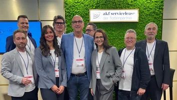 Gruppe von acht Personen mit Namensschildern steht vor grünem Wandpaneel mit Schild akf servicelease der flottenpartner und zwei Bildschirmen