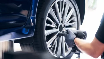 Hand mit Handschuh bedient Schlagschrauber an Felge eines blauen Autos