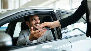 Mann im Auto reicht Schlüssel an stehende Person