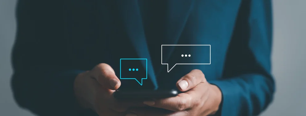Hände halten ein Smartphone mit zwei Sprechblasen-Symbolen darüber