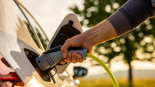 Nahaufnahme einer Hand, die gerade den Stecker zum Aufladen eines E-Autos in Auto einsteckt