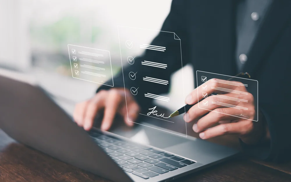 Hand einer Person, die mit einem Stift auf einem Laptop eine digitale Unterschrift auf einem virtuellen Dokument setzt
