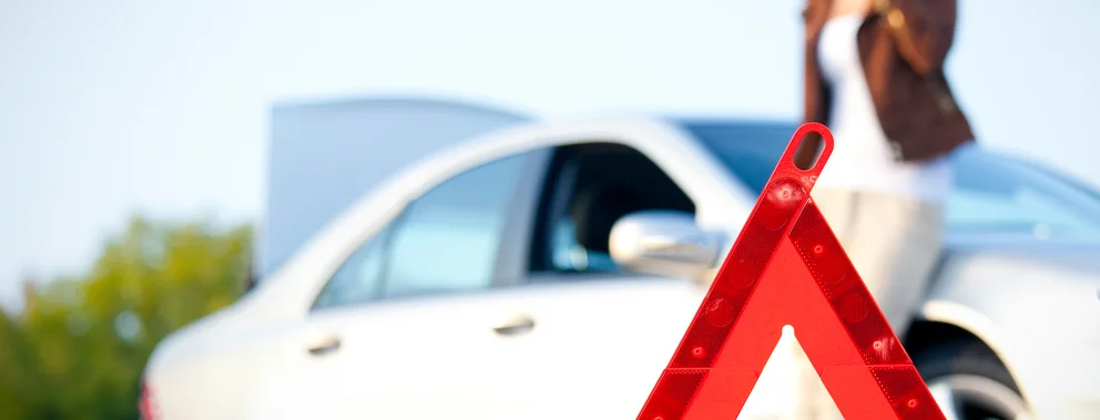 Rotes Warndreieck vor einem weißen Auto auf einer Straße