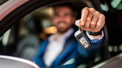 Person im Anzug hält Autoschlüssel aus geöffnetem Autofenster heraus