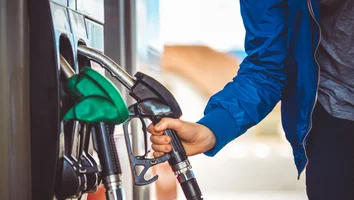 Hand in blauer Jacke hält Zapfpistole an Tankstelle