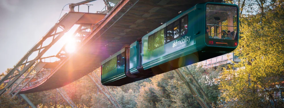 Schwebebahn mit Sonnenlicht im Hintergrund über einem bewaldeten Tal
