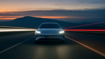 Elektroauto mit eingeschalteten Scheinwerfern fährt auf einer Straße bei Dämmerung mit Berg im Hintergrund