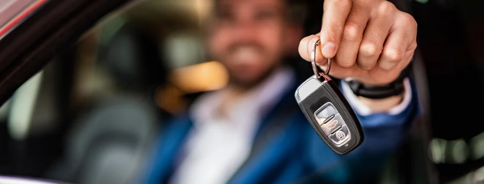 Person im Anzug hält Autoschlüssel aus geöffnetem Autofenster heraus