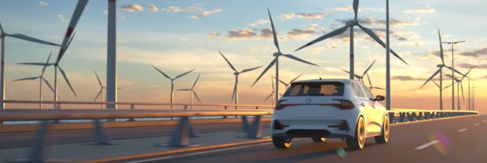 Ein weißes Auto fährt auf einer Brücke mit Windrädern im Hintergrund bei Sonnenuntergang