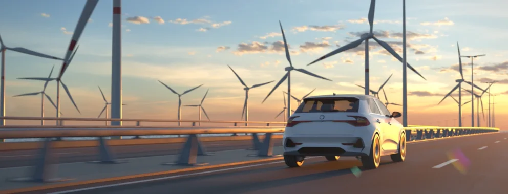 Ein weißes Auto fährt auf einer Brücke mit Windrädern im Hintergrund bei Sonnenuntergang