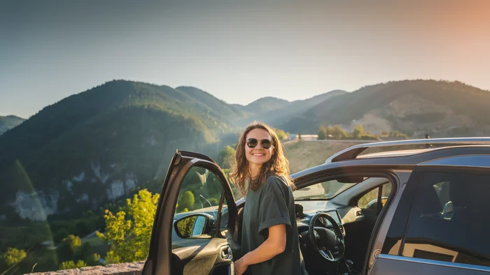 Eine Frau steigt aus einem Auto aus, im Hintergrund is eine Berglandschaft zu sehen