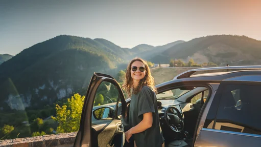 Eine Frau steigt aus einem Auto aus, im Hintergrund is eine Berglandschaft zu sehen