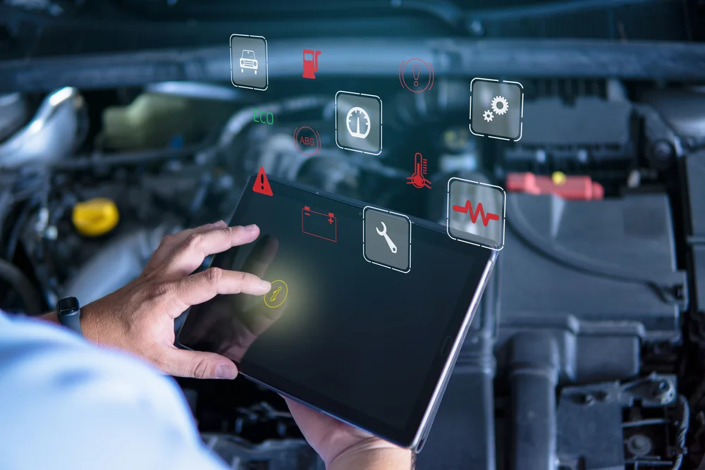 Hand hält Tablet vor geöffnetem Motorraum mit schwebenden Symbolen für Fahrzeugdiagnose